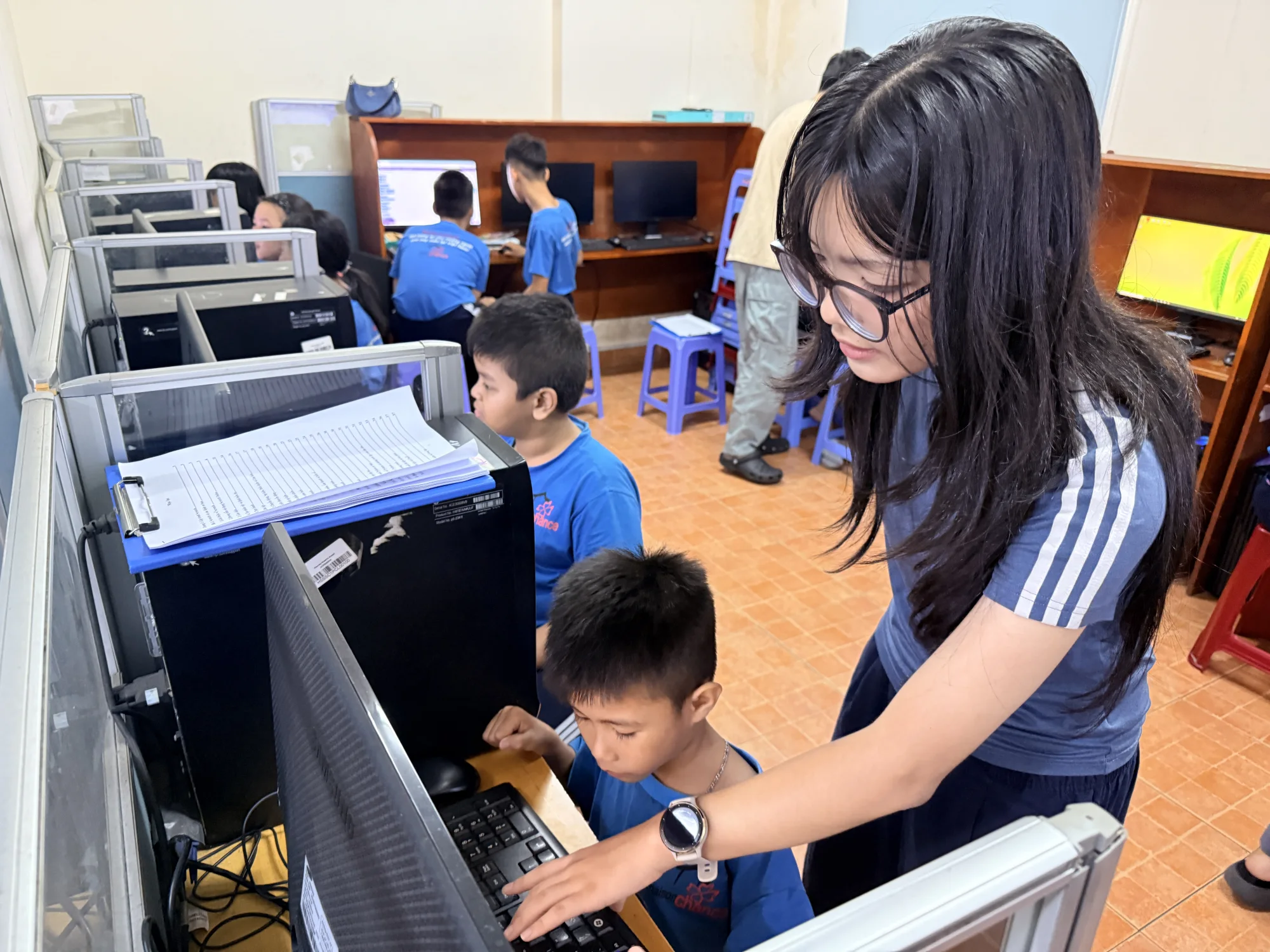 Ngân helping a young learner use a computer